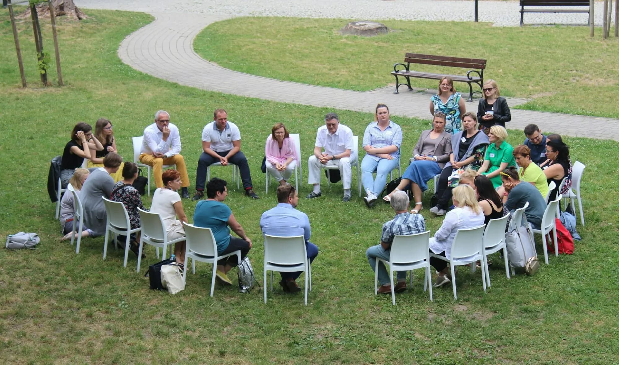 People sit in a circle of chairs on a lawn for an outdoor community gathering